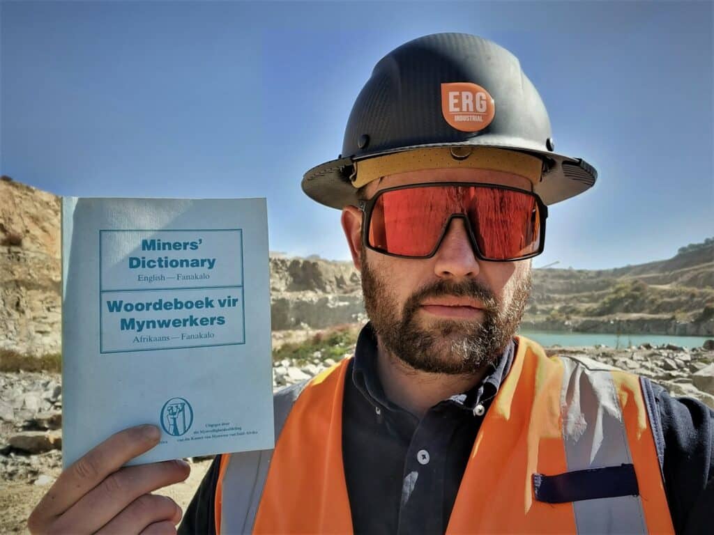 Eugene the MD of ERG Industrial holding up a blue miners dictionary, on a construction site with an ERG industrial hat.