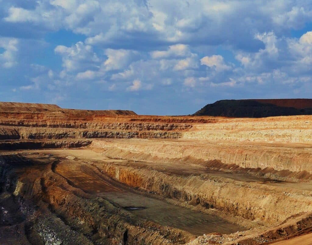 A large open-pit mining operation with engineered terracing, exposed geological layers, and the vastness of the operation.