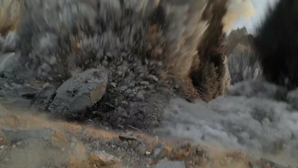The dynamic moment of an explosion within a quarry or construction site throwing rocks and debris into the air.