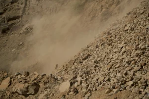 Post-blast dust cloud rising above a fragmented rock bench at Mine A, South Africa