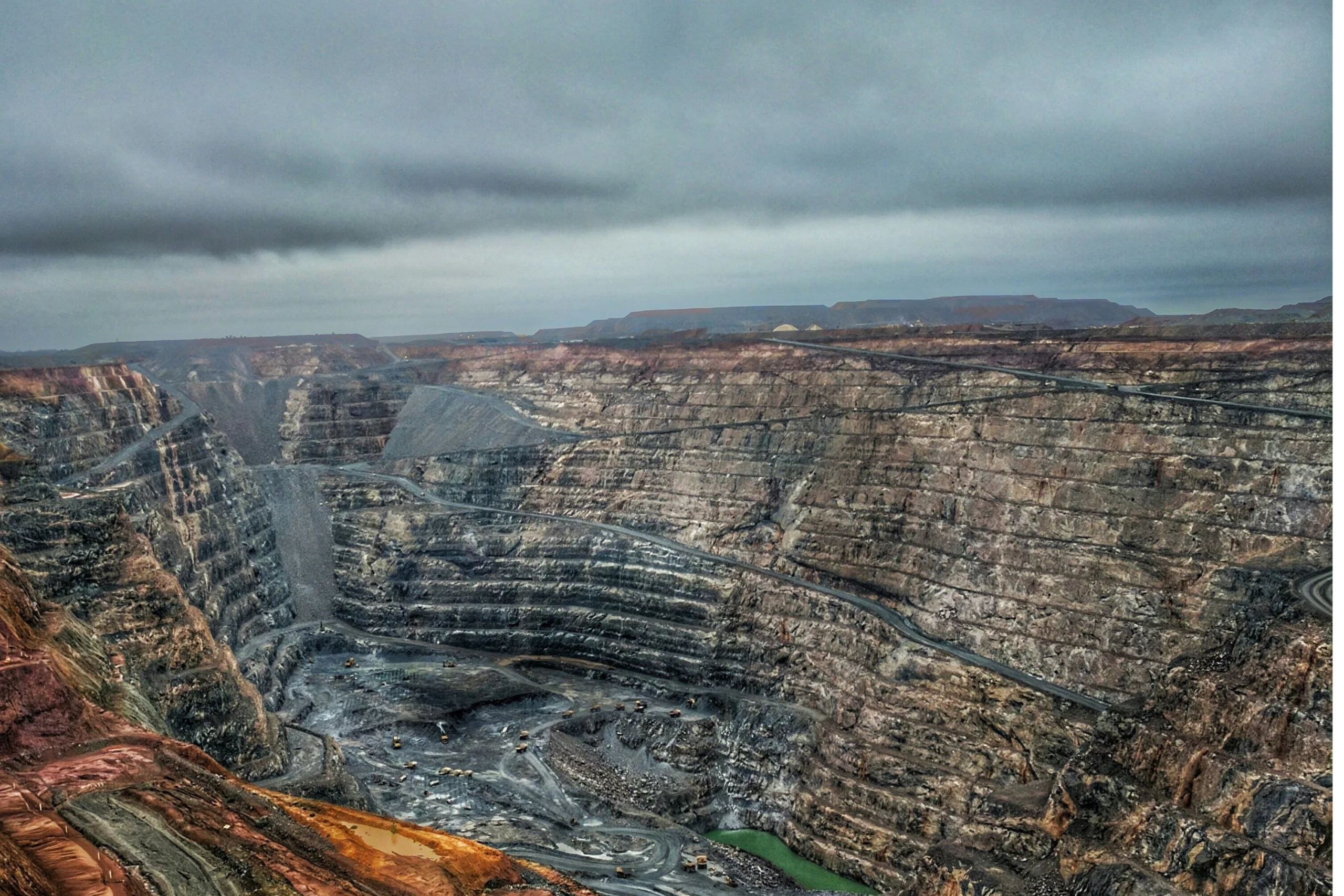 Open-cut mine with exposed rock faces and bench levels typical of drill-and-blast operations