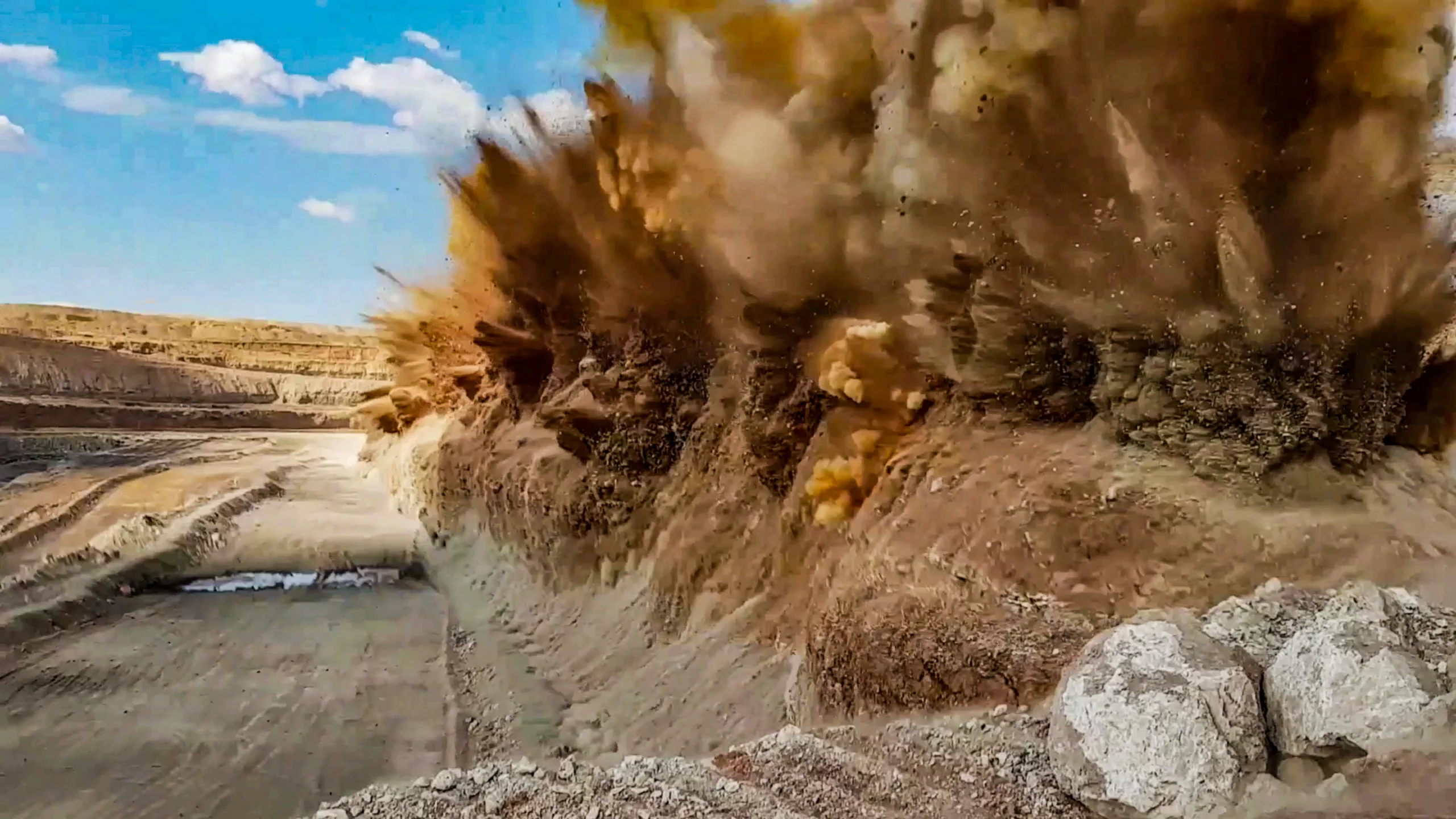 Articles 2 A controlled blast detonating along a bench in an open-pit mine, sending rock and dust into the air above the quarry face.